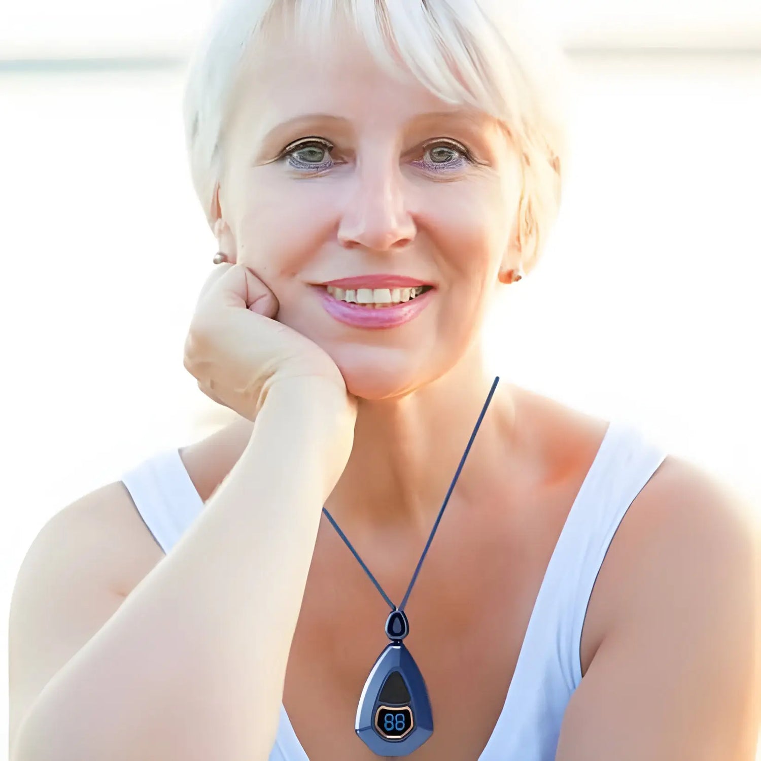 Femme souriante d’âge moyen aux cheveux blonds courts, portant un haut blanc et un collier à pendentifs bleu.