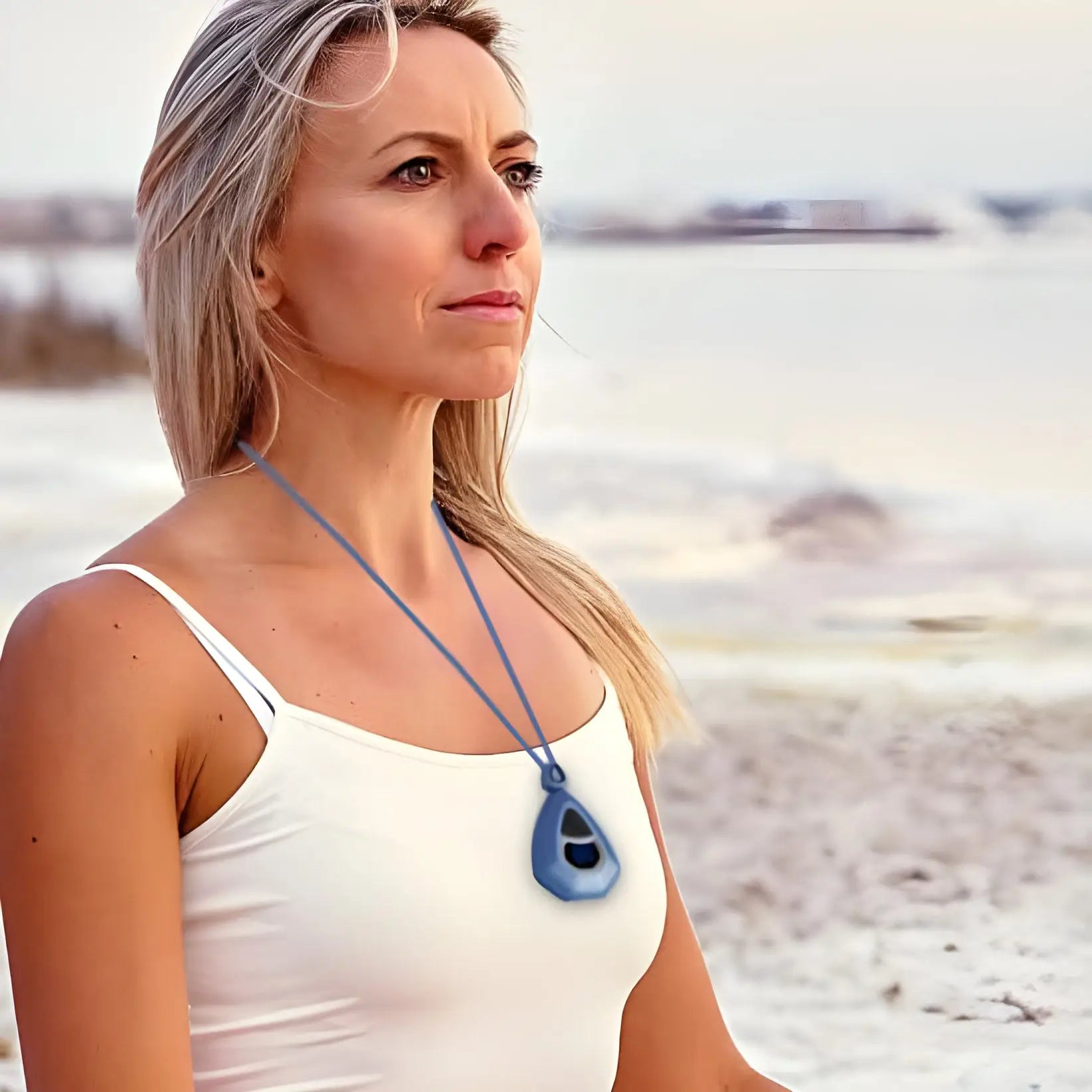 Femme aux longs cheveux blonds portant un débardeur blanc et un collier à pendentifs bleu.