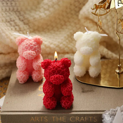 Trois bougies décoratives en forme d’ours en peluche de couleur rouge, rose et blanche avec des surfaces texturées.