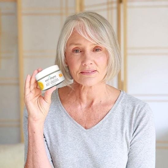 Pot de produit de soin tenu par une femme d’âge mûr aux cheveux gris courts.