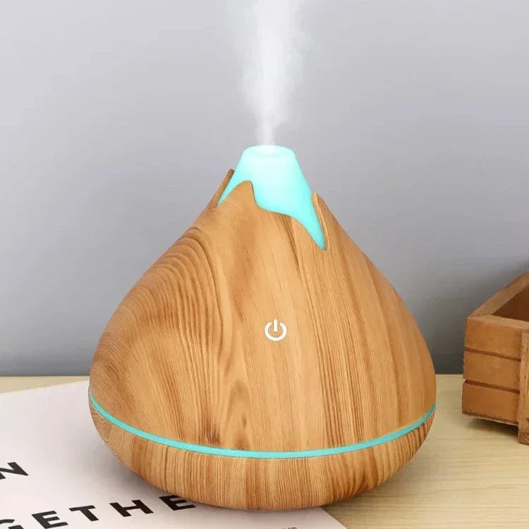 Diffuseur d’huiles essentielles en bois en forme de goutte d’eau avec des accents turquoise émettant de la vapeur.