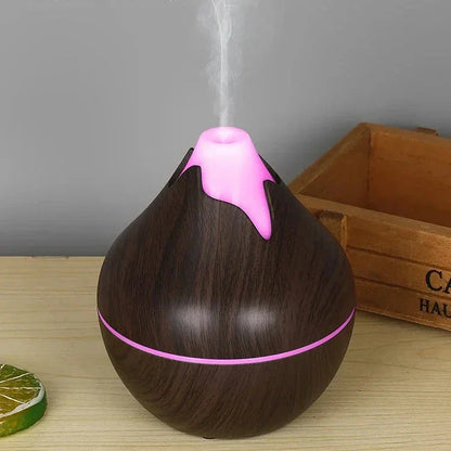 Diffuseur d’huiles essentielles en bois foncé avec éclairage LED rose émettant de la vapeur.