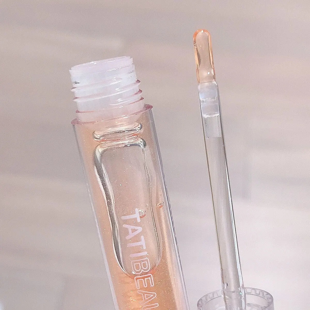 Tube de gloss transparent avec applicateur en forme de baguette.