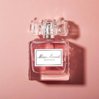 Flacon de parfum rose avec un bouchon en cristal en forme de noeud, étiqueté ’Miss Sweet’.