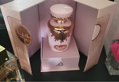 Flacon de parfum rose avec des accents décoratifs en forme de soleil doré dans un élégant coffret de présentation.