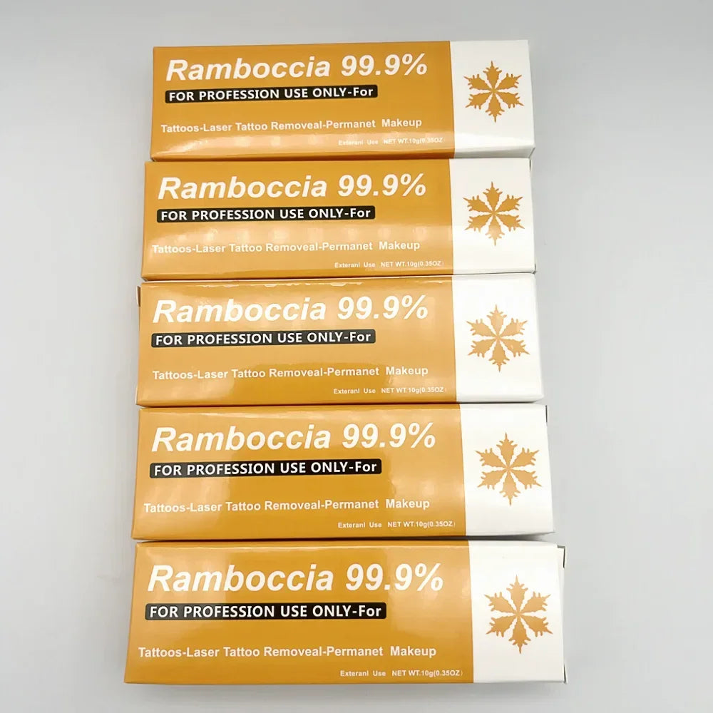 Cinq boîtes empilées de produit de détatouage Ramboccia 99,9 % à usage professionnel avec un emballage or/orange.